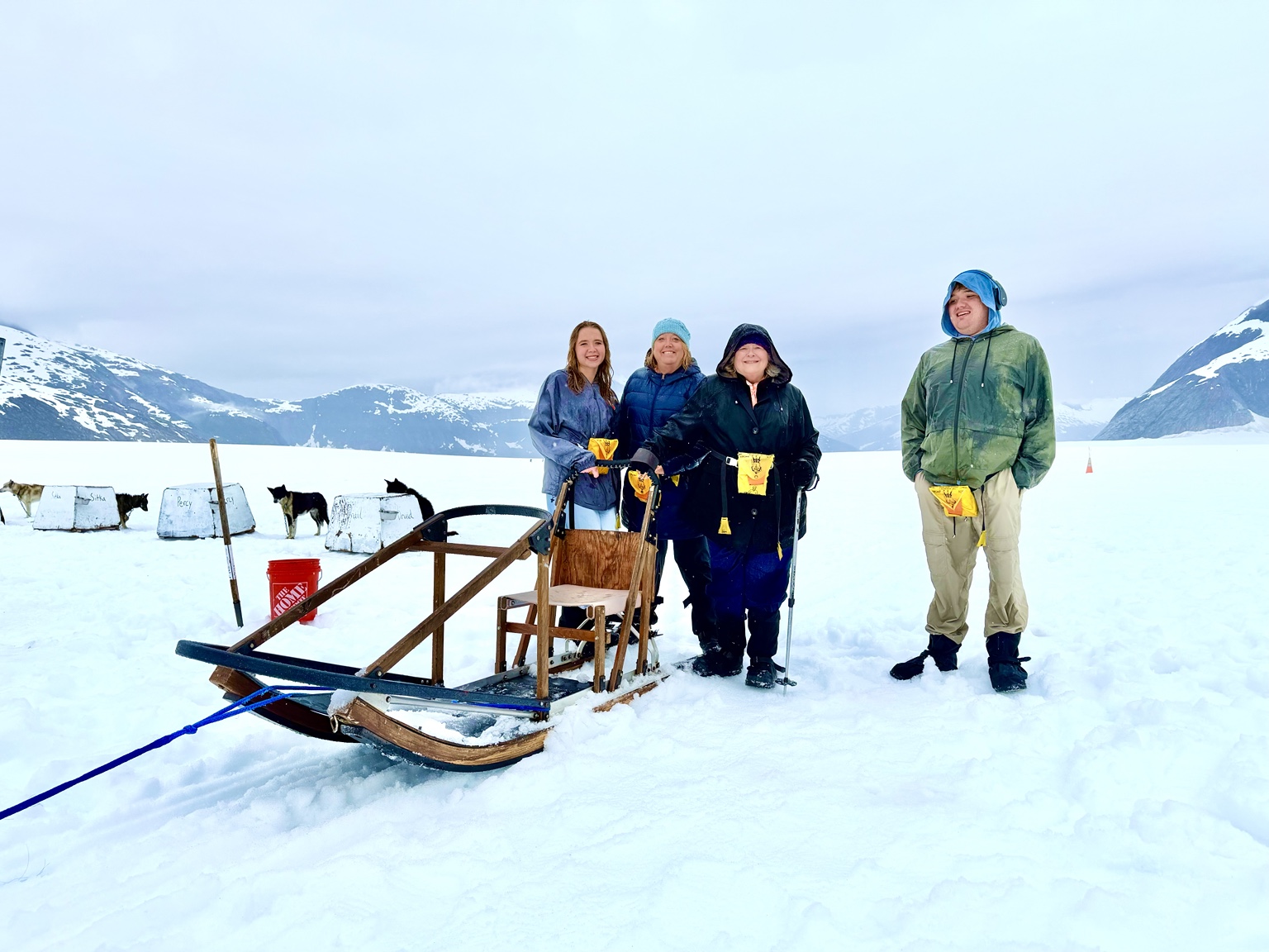 Our family standing beside a dog sled on a snowy glacier, with a mobility cane and sled dogs nearby