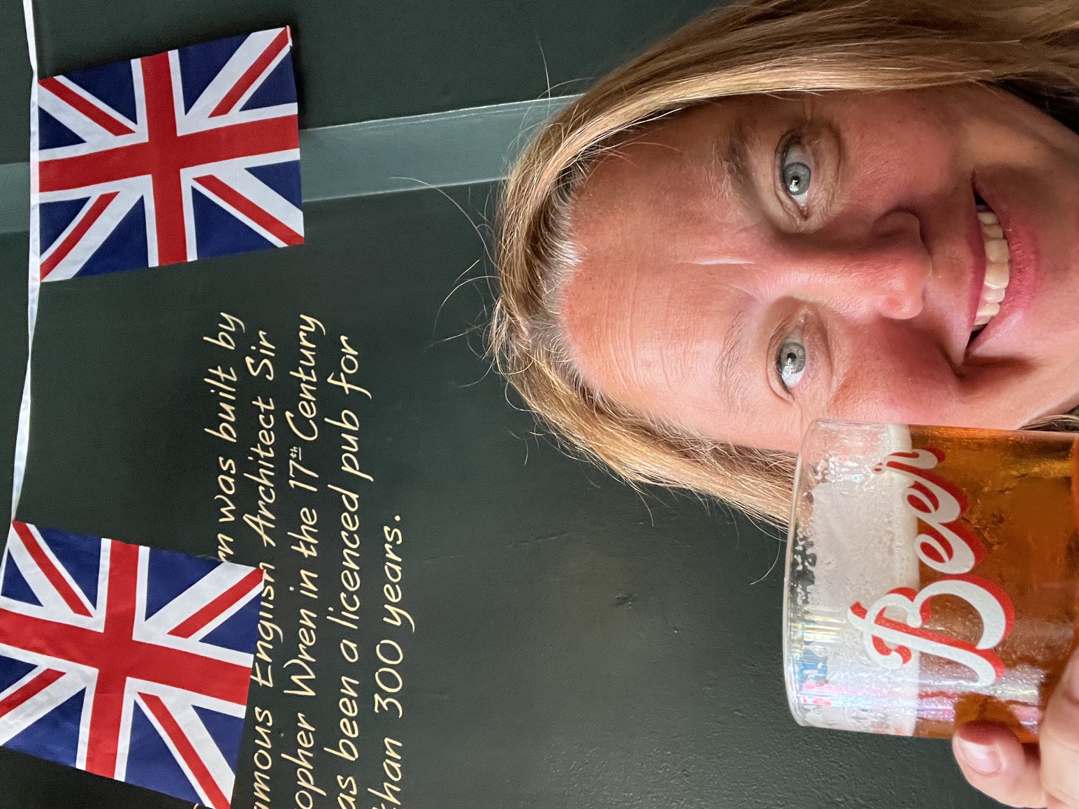 Christine Scheeler holding a pint in a historic London pub decorated with Union Jack bunting