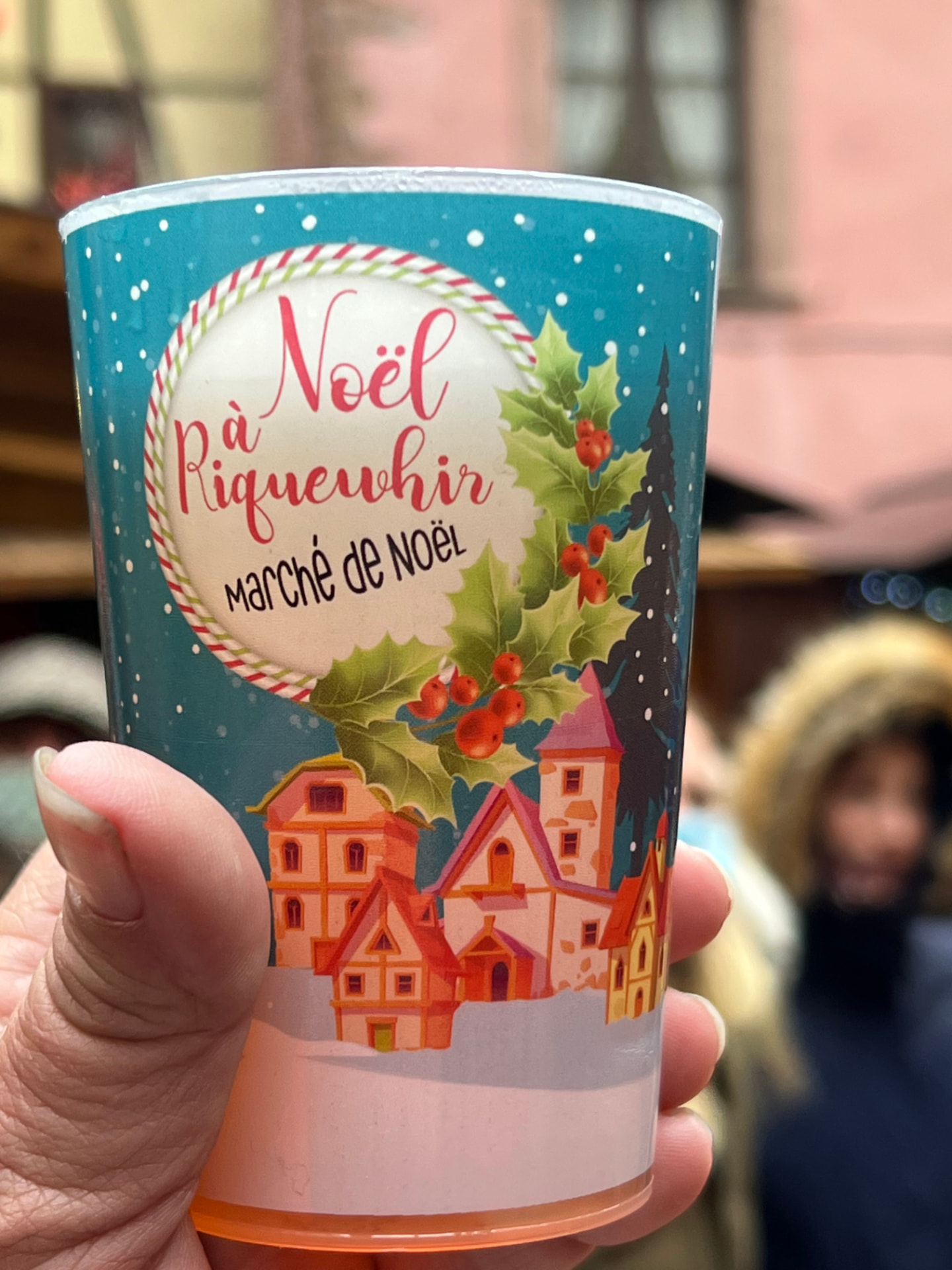 A No&euml;l &agrave; Riquewihr souvenir mulled wine cup held up at the Christmas market