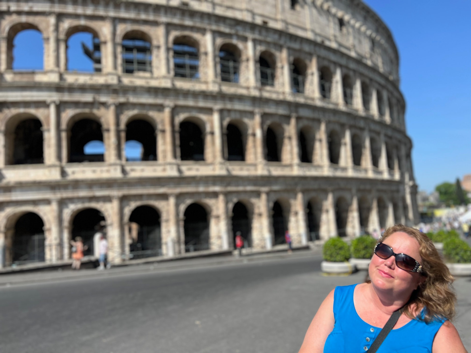 The Colosseum in Rome under a clear blue sky, with Christine Scheeler standing in the foreground