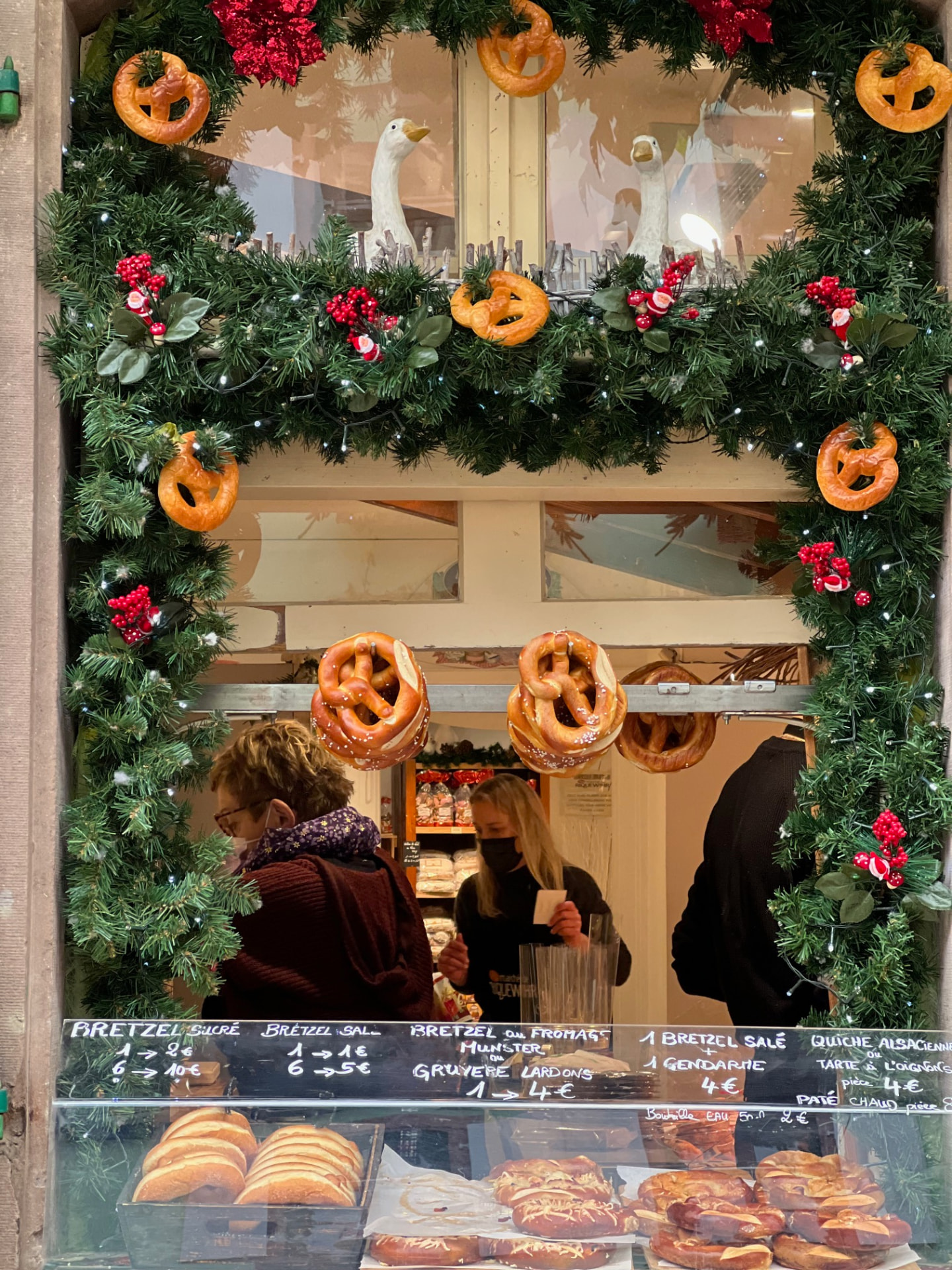 A pretzel stand framed by Christmas garland and lights at a market in Riquewihr, France