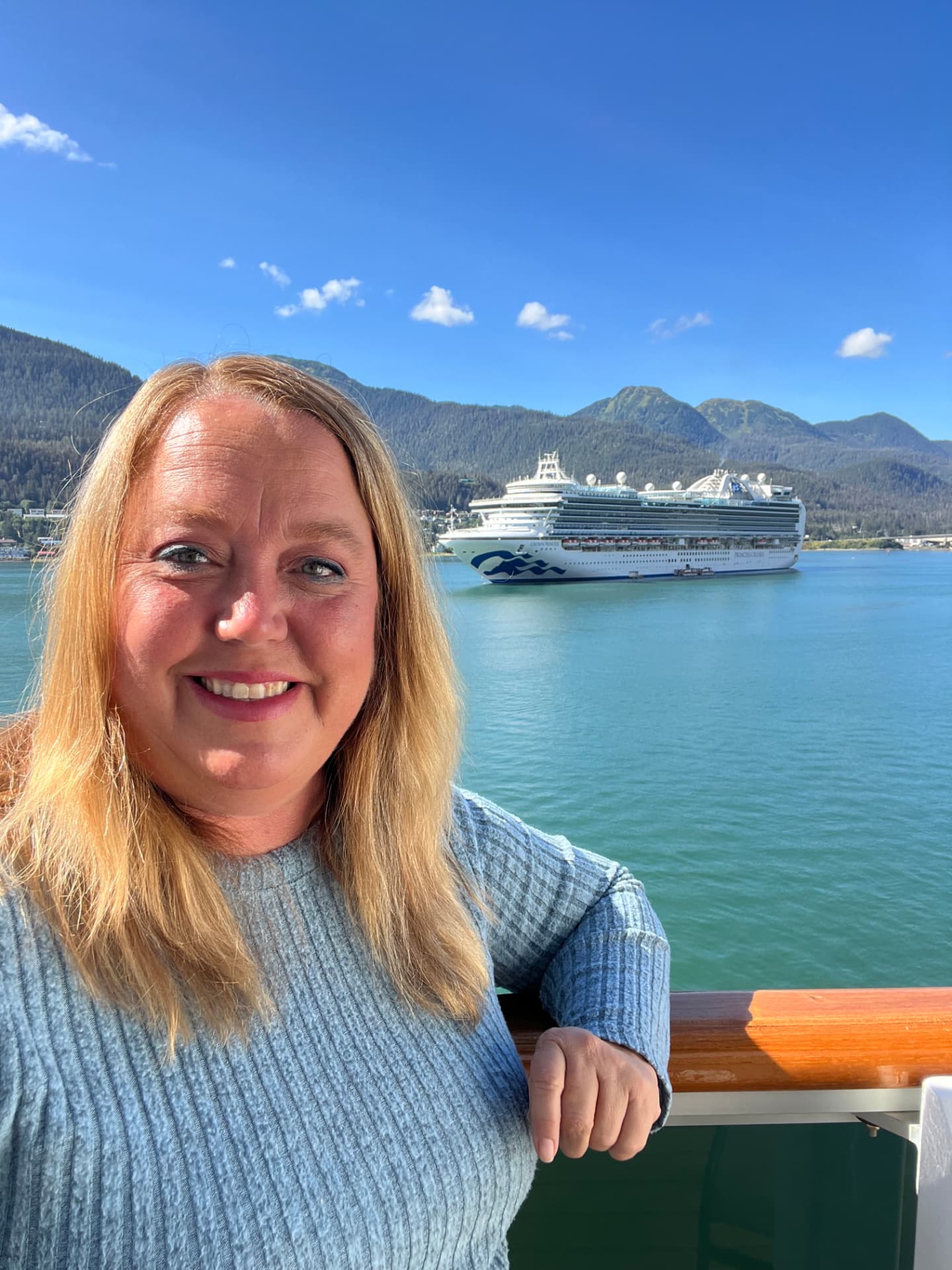 Christine at a ship railing in Alaska with a Princess Cruises ship and forested mountains behind her