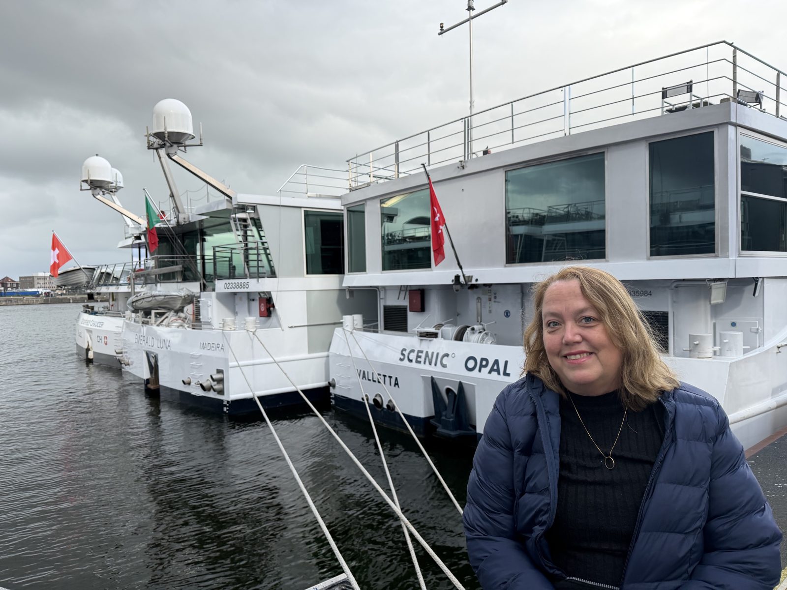 Christine Scheeler on a dock beside river ships moored side by side, including Scenic Opal